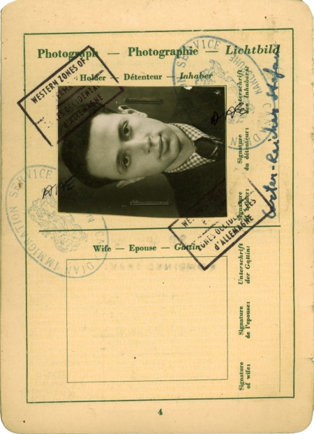 Beige-coloured page of an official document containing several stamps, signatures, and handwriting. One page includes a black-and-white portrait of a young man with combed-back hair and a suit and tie, positioned sideways on the top of the page.