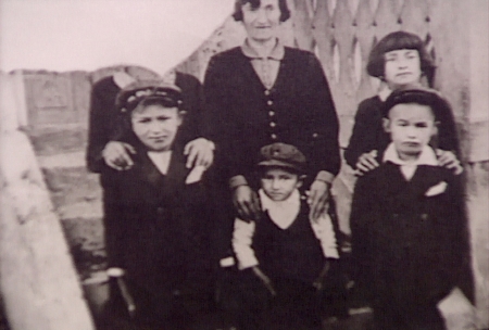 Photo en noir et blanc d'une femme avec cinq enfants se tenant debout, les trois qui sont dans la rangée arrière ont leurs mains sur les épaules de leurs proches. La photo est déchirée dans le coin supérieur gauche de manière à ce que le visage de la personne qui est dans ce coin ne soit pas visible.