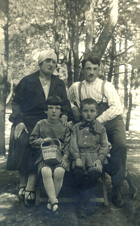 Photo en noir et blanc d'une famille de quatre, rassemblés ensemble pour une photo extérieure, entourés d'arbres. L'homme et la femme se tiennent derrière leur deux enfants assis.