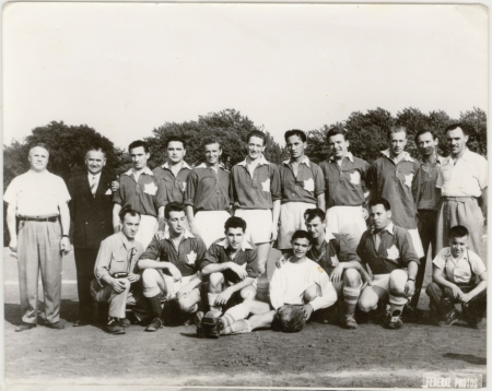 Photo en noir et blanc d'une équipe de soccer d'environ 15 jeunes hommes et quatre entraîneurs, répartis en deux rangées sur un terrain de soccer. Leur uniforme d'équipe présente un drapeau canadien sur leur poitrine.