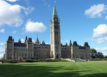 Color photo of the Canadian parliament central building with green grass at the front and a blue sky with a couple of clouds.