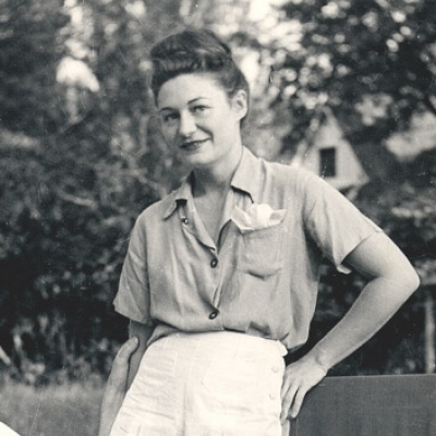 Black and white photo of a woman standing in a garden. She wears shorts and summer clothes.