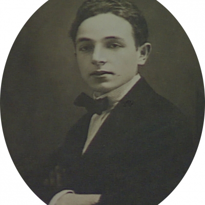 Photo en noir et blanc de forme ovale, prise en studio, d'un jeune homme. L'homme porte un complet avec un nœud papillon. La photo a une grande bordure blanche.