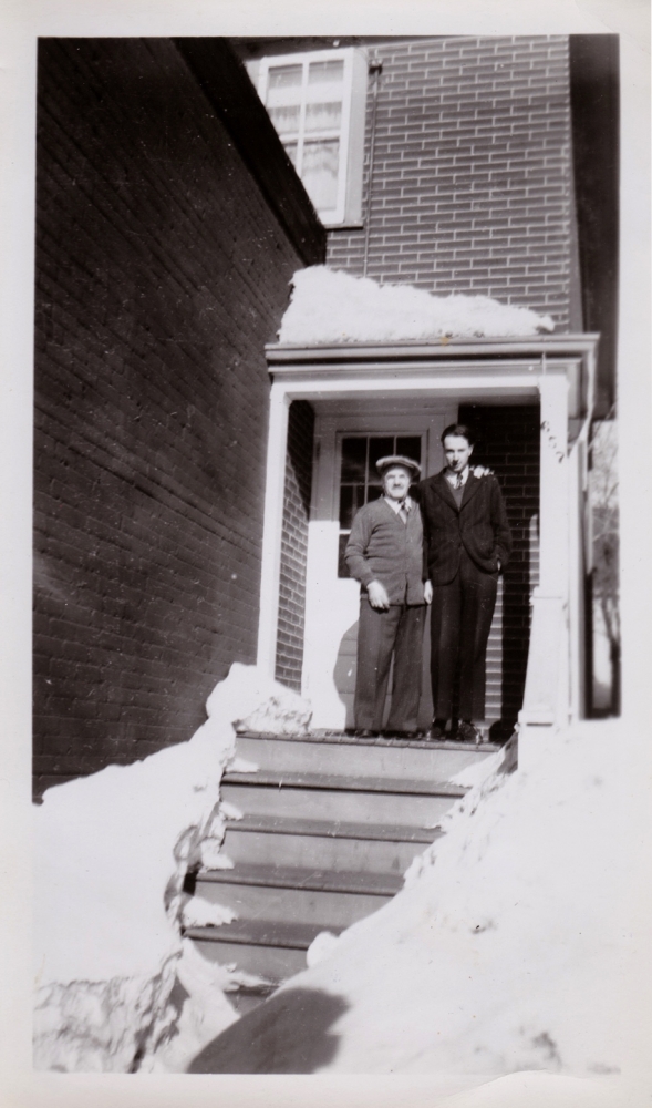 Photo en noir et blanc de deux hommes debout ensemble à l'extérieur d'un maison pendant l'hiver.