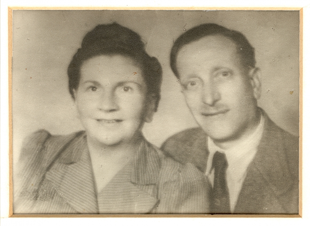 Photo en noir et blanc prise à partir du buste, d'un homme et d'une femme souriant à la caméra. L'homme porte costume et cravate et la femme a les cheveux attachés.