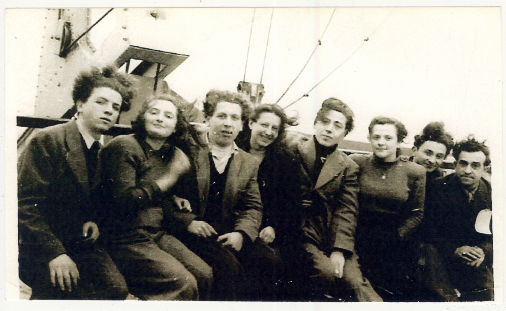 Black-and-white photograph of a group of 8 young adults, men and women, sitting together on the deck of a ship.