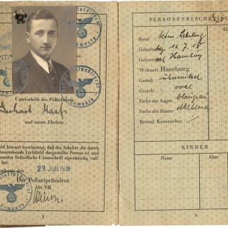 Two pages of a passport with blue stamps and black handwriting. The left page features a black-and-white identity photograph of a young man wearing a suit and tie.