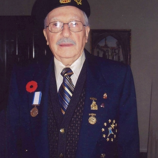 Photo en couleur d'un homme âgé portant un uniforme militaire et souriant à la caméra. Son veston et son béret sont décorés de médailles et d'épinglettes et d'un coquelicot du Jour du souvenir.