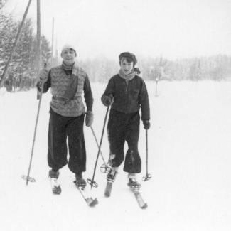 Photo en noir et blanc d'une femme et d'un jeune garçon portant des vêtements d'hiver et faisant du ski de fond sur un terrain enneigé.