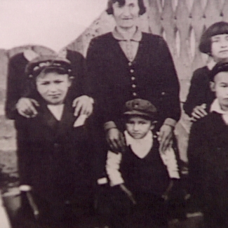 Photo en noir et blanc d'une femme avec cinq enfants se tenant debout, les trois qui sont dans la rangée arrière ont leurs mains sur les épaules de leurs proches. La photo est déchirée dans le coin supérieur gauche de manière à ce que le visage de la personne qui est dans ce coin ne soit pas visible.