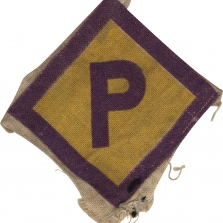 Photo en couleur d'un badge en tissu en forme de losange. Le centre est jaune avec des bordures de couleur pourpre. Il y a la lettre “P” de couleur pourpre en majuscule au centre du badge.