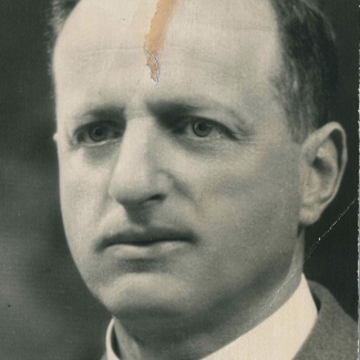 Black-and-white portrait photograph of a man, photo taken from his shoulders up. He is wearing a suit and tie.