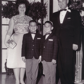 Photo en noir et blanc d'un homme et d'une femme avec leurs deux fils. La famille est vêtue de manière formelle et l'homme ainsi que les garçons portent des complets avec des nœuds papillons et la femme porte une robe.