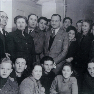 Black-and-white photograph of a large group of about thirty youth, grouped in two rows and smiling at the camera. An older man in a suit stands in the middle of the group.