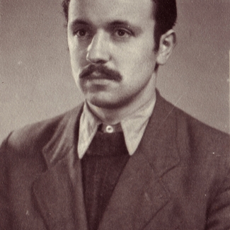 Sepia-toned portrait photograph of a man, pictured from the chest up, looking towards the left of the camera. He wears a suit and tie, and his hair is combed back. He has a moustache.