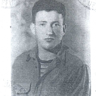 Black-and-white identity photograph of a young man, pictured form chest up, looking at the camera. He has dark brown hair, and wears a collared shirt over a striped t-shirt.