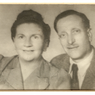 Black-and-white photograph of the bust of a man and woman smiling at the camera. The man wears a suit and tie, and the woman has her hair up.