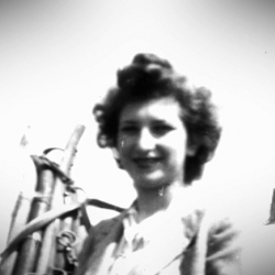 Black-and-white photograph of a woman smiling at the camera, standing beside a white horse with her hand resting on the horse’s reigns.