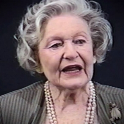 Screenshot of Holocaust survivor Irene Burstyn video testimony. She is sitting in front of a black background, and looking to the left of the camera. The camera shows her face and shoulders.