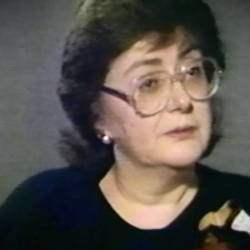 Screenshot of Holocaust survivor Freda Shiel, sitting in front of a grey background, and looking to the right of the camera while recording her video testimony. The camera shows her face and shoulders.