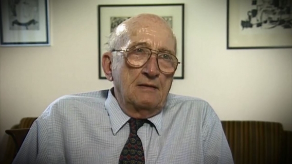 Screenshot of Holocaust survivor Gerhart Maass video testimony. He is sitting in front of a wall with three paintings, and looking to the right of the camera. The camera shows his face and shoulders.