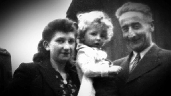 Black-and-white photograph of a woman, standing beside a young boy with blonde curly hair hold by a man at her left.