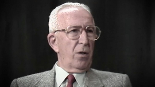 Screenshot of Holocaust survivor Jack Hahn video testimony. He is sitting in front of a dark background, and looking to the right of the camera. The camera shows his face and shoulders.