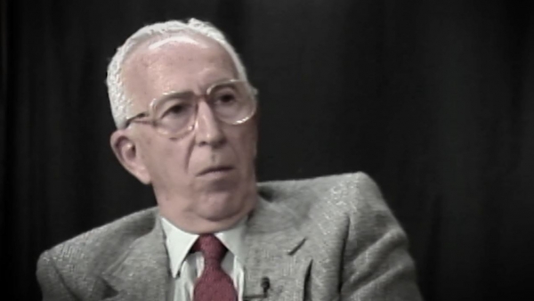 Screenshot of Holocaust survivor Jack Hahn video testimony. He is sitting in front of a dark background, and looking to the right of the camera. The camera shows his face and shoulders