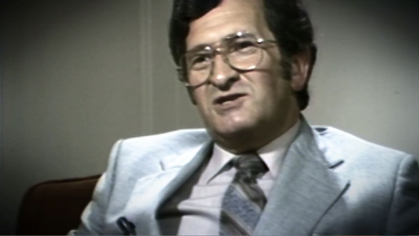 Screenshot of Holocaust survivor David Mark testimony video. He is sitting in front of a grey background, and looking to the left of the camera. The camera shows his face and shoulders.