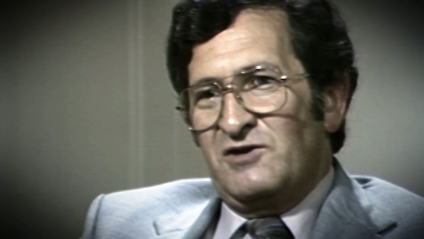 Screenshot of Holocaust survivor David Mark testimony video. He is sitting in front of a grey background, and looking to the left of the camera. The camera shows his face and shoulders.