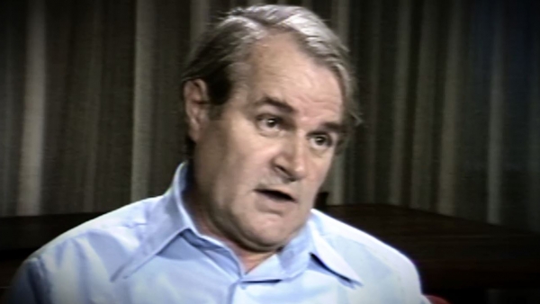 Screenshot of Holocaust survivor Aba Beer video testimony. He is sitting in front of grey curtains, and looking to the right of the camera. The camera shows his face and shoulders.