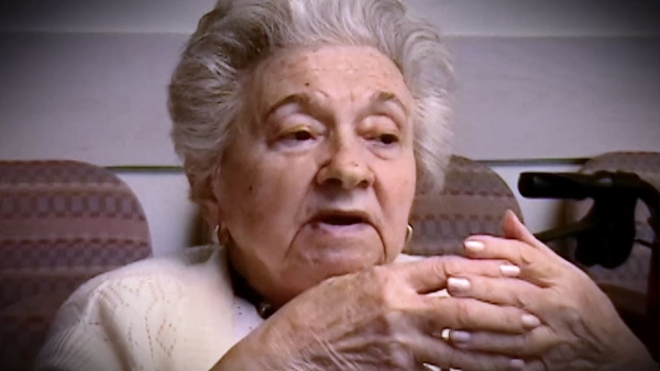 Screenshot of Holocaust survivor Mania Kay video testimony. She is sitting in front of a black background, and looking to the right of the camera. The camera shows her face and shoulders.