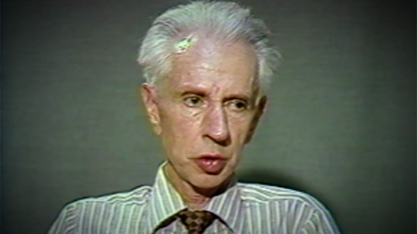 Screnshot of Holocaust survivor Stefan Carter video testimony. He is sitting in front of a dark background and looks to the right of the camera. The camera shows his face and shoulders.